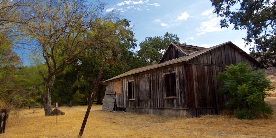 Dilapadated brown wooden house surrounded by trees and blue sky