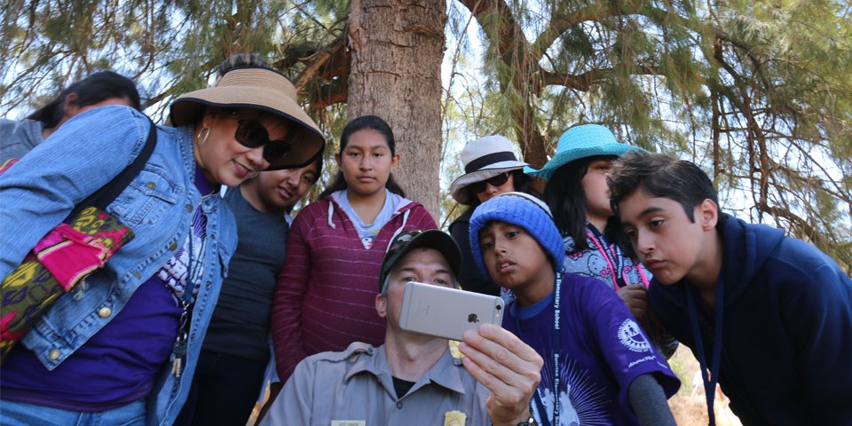 A group of young people gather around a ranger to look at a smartphone A group of young people gather around a ranger to look at a smartphone