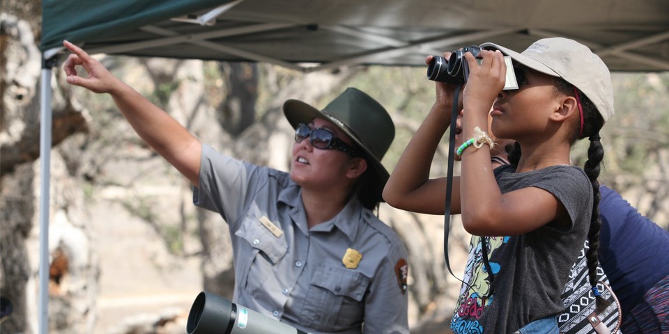 A youth looks through binoculars while a ranger points