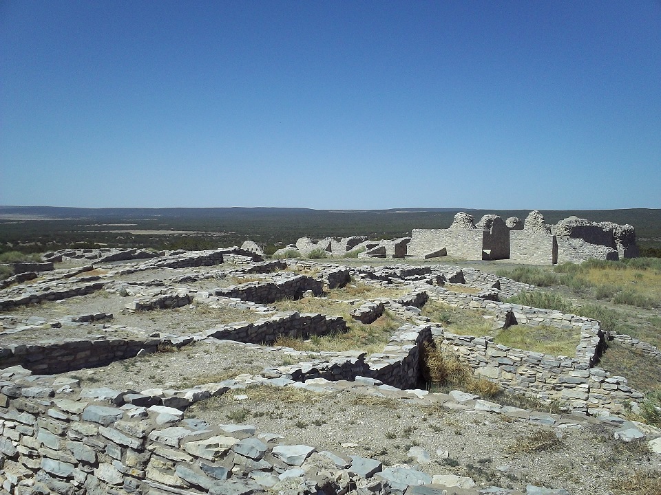 The ruins of a Puebloan houseblock and 17th century Spanish mission church under a clear blue sky.