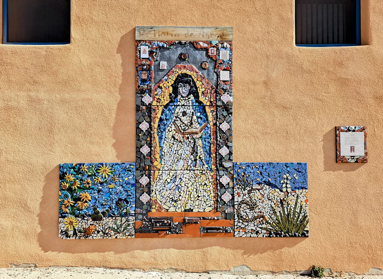 Maria de Agreda Mural in Mountainair New Mexico three panel tile mural on a adobe wall. flanking a woman in robes are two desert scense