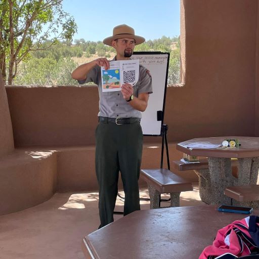 Park Guide Alex Giving a Bark Ranger Program A park ranger stands in front of an audience holding an activity sheet.