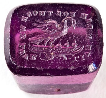 A small, translucent purple cube-shaped object with Latin phrase engraved in reverse on one face.