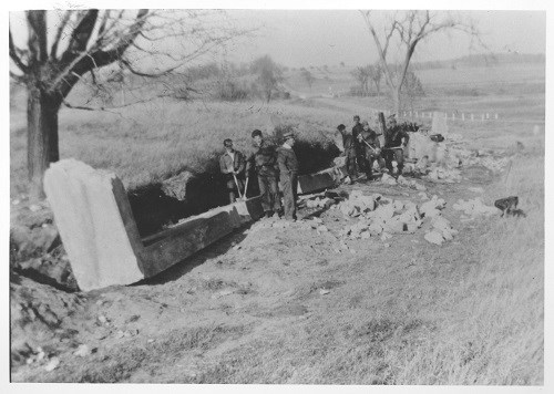 Crew of several young men with hand tools working on removing a concrete foundation.