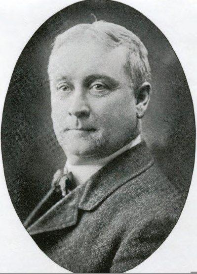 Middle aged man with short hair, bow tie, and a tweed suit.