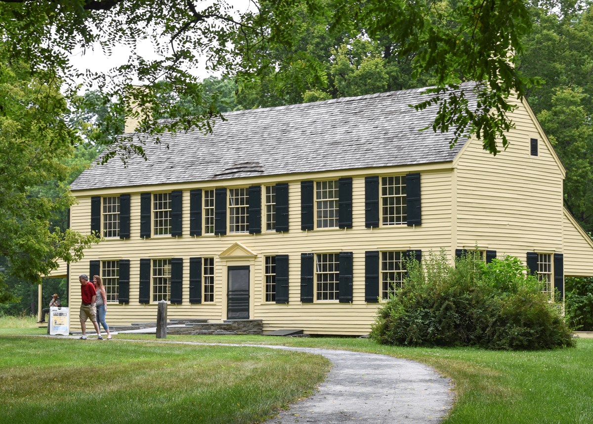 Visitors walk past a historic, yellow, two story house