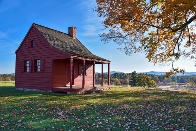 A red historic house next to fall trees.