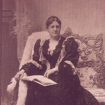 Middle aged woman in an ornate dress and seated on a chair with an open book on her lap.