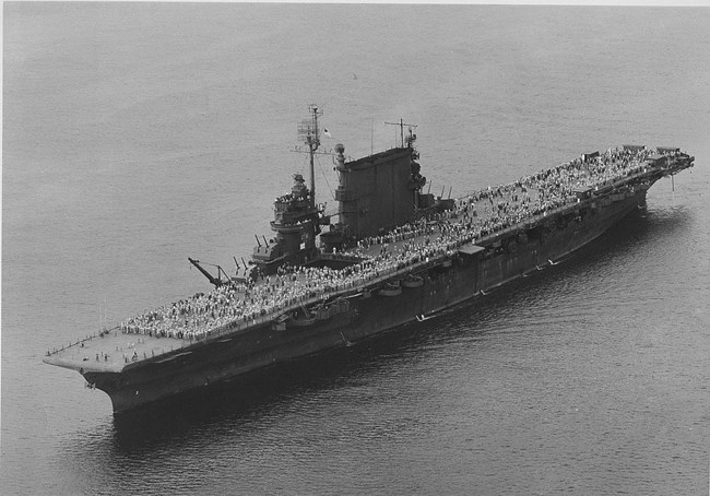 A huge crowd of veterans stand on a ship's deck as it floats on the open ocean.
