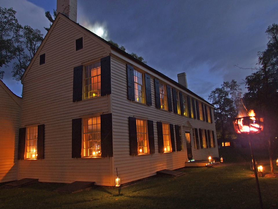 front of historic yellow house lit by candlelight