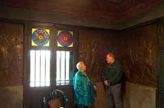 View inside the main chamber of Saratoga Monument.  A man and woman talk in the corner near several large, somewhat dark bronze plaques.