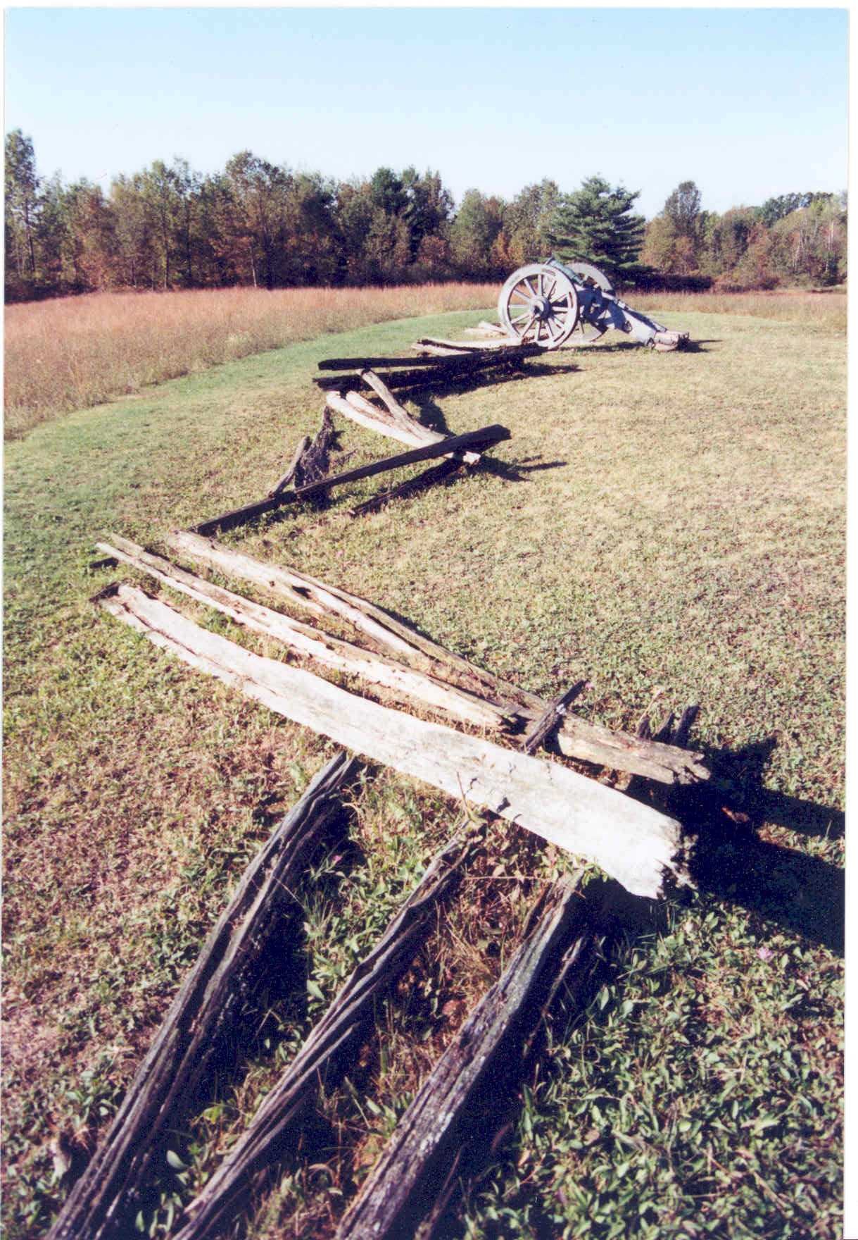 A wooden fence runs into the distance, separating two fields. A cannon sits in the distance next to the fence.