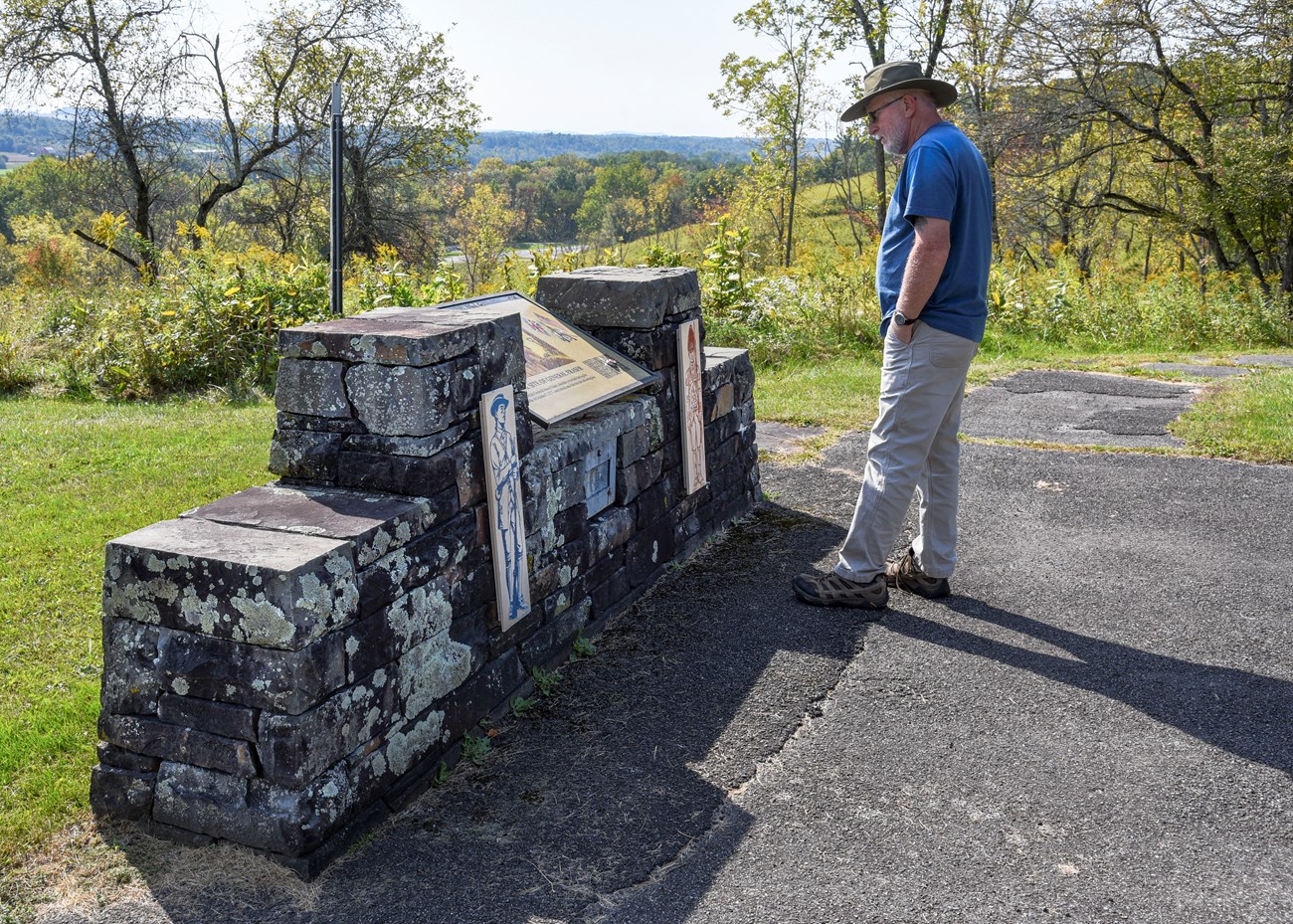 A visitor reads a stone wayside at the Fraser Memorial