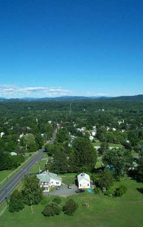 View from the top of Saratoga Monument, looking east.  A road runs from the lower left corner of the view fairly well straight into the distant green hills.  Deep blue skies drop about halfway down the view, and a few clouds sit on the horizon.