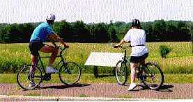 Two bicyclists stop to read a sign describing the scene in front of them. Two bicyclists stop to read a sign describing the scene in front of them.