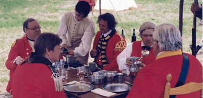 Several British officers sit down to a meal in camp. A young man serves the meal. Several British officers sit down to a meal in camp. A young man serves the meal.