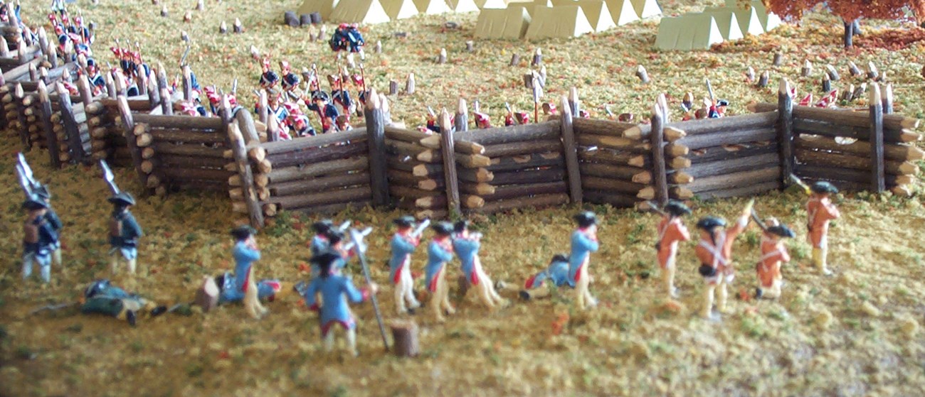Model figures of soldiers along a tall, wooden, zig-zagged fence