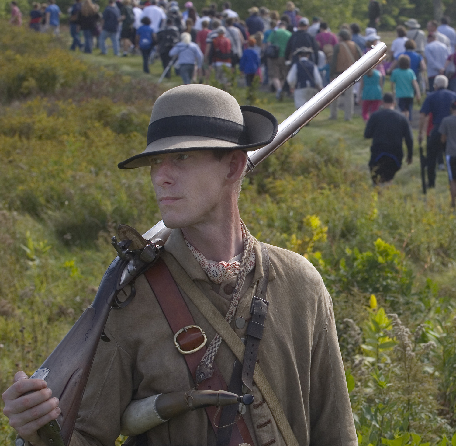 Colonial soldier holding musket, crowd of visitors in background Colonial soldier holding musket, crowd of visitors in background