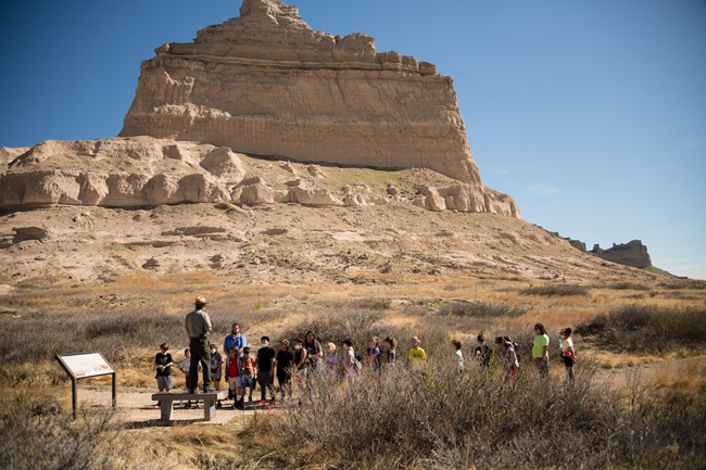 A park ranger talks to a group of students in front of a sandstone formation.