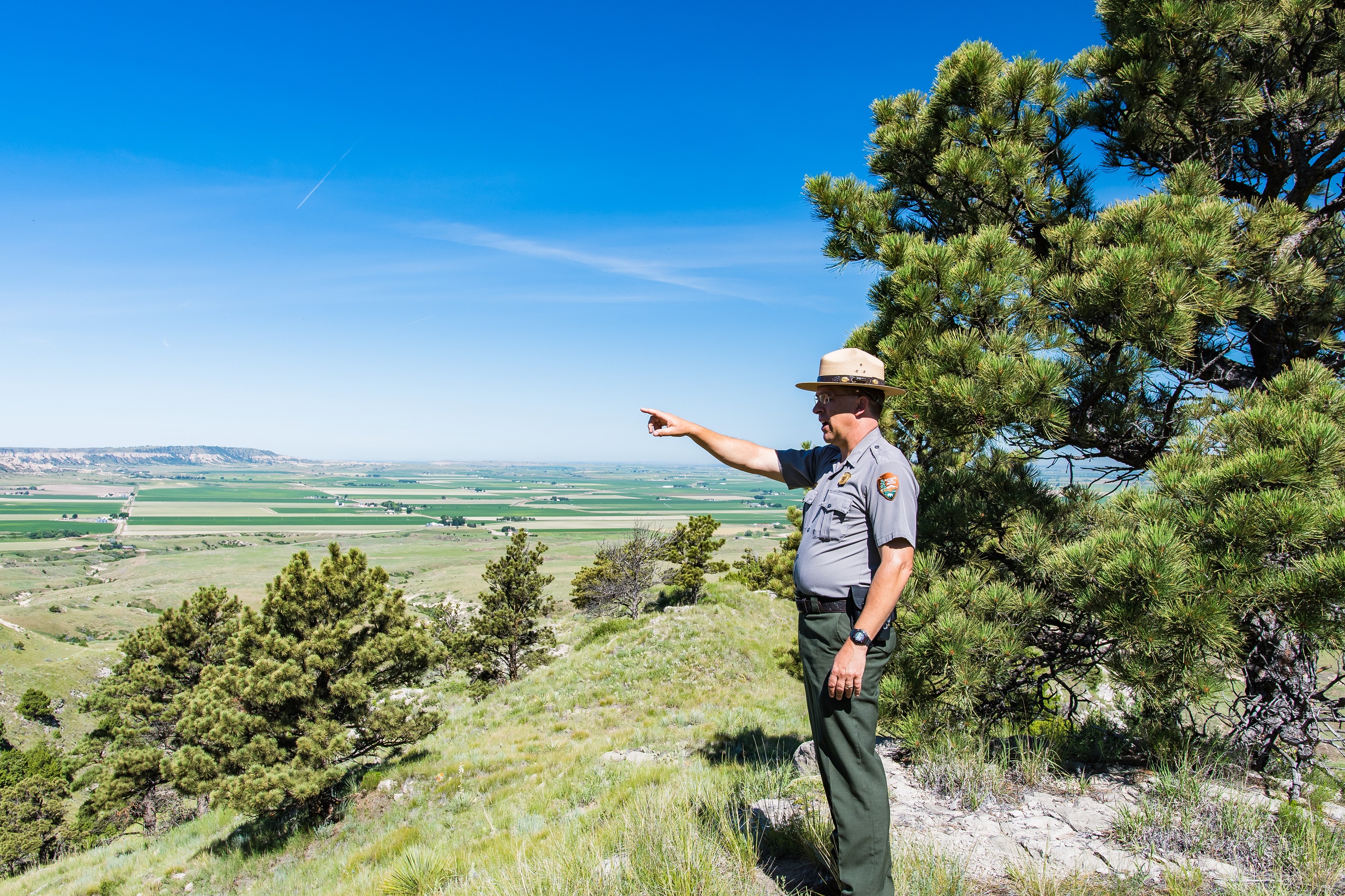 Matt Salomon A stands on the top of a prominent landform, pointing to his right.