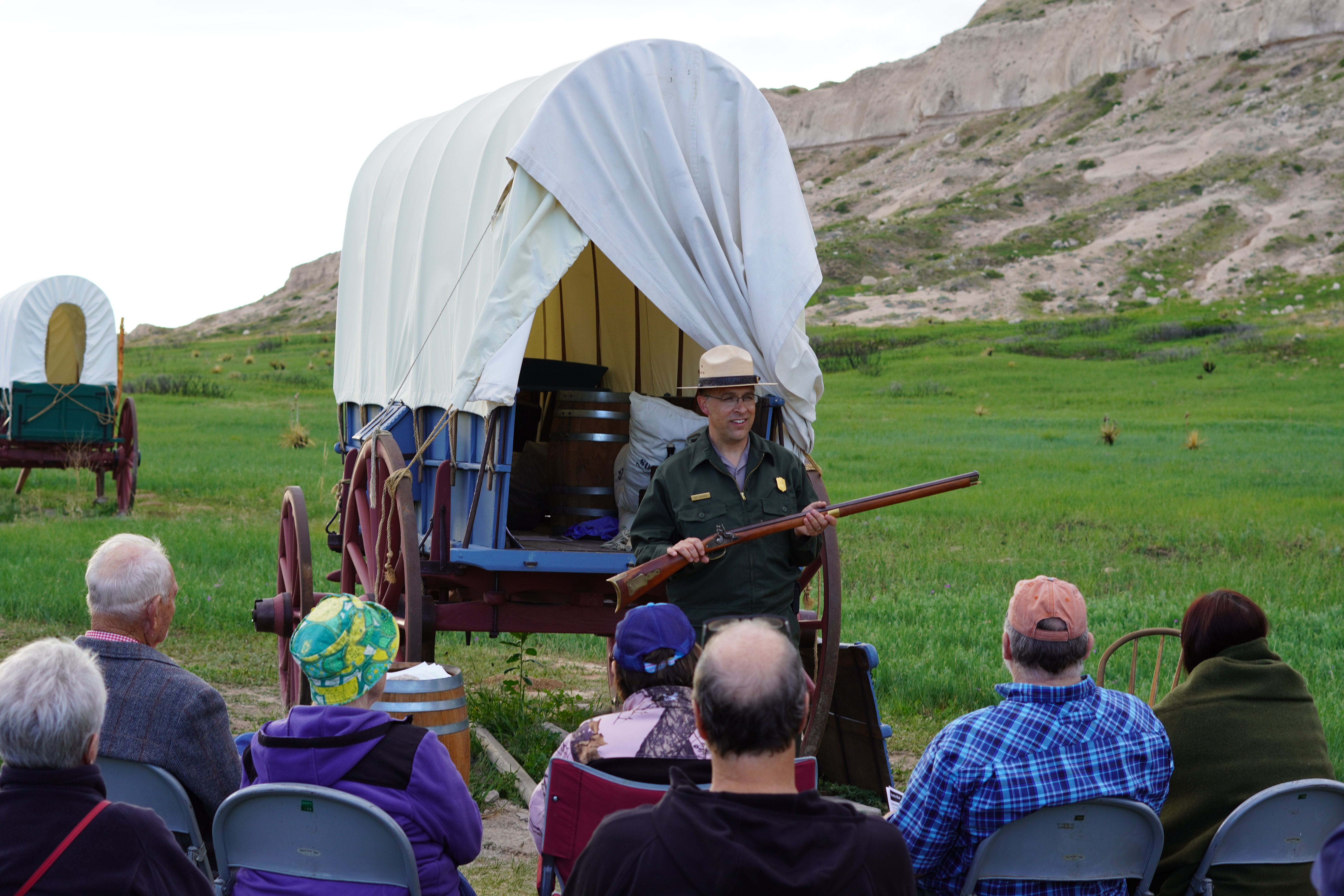 A park ranger holds a historic rifle while he talks to an audience.