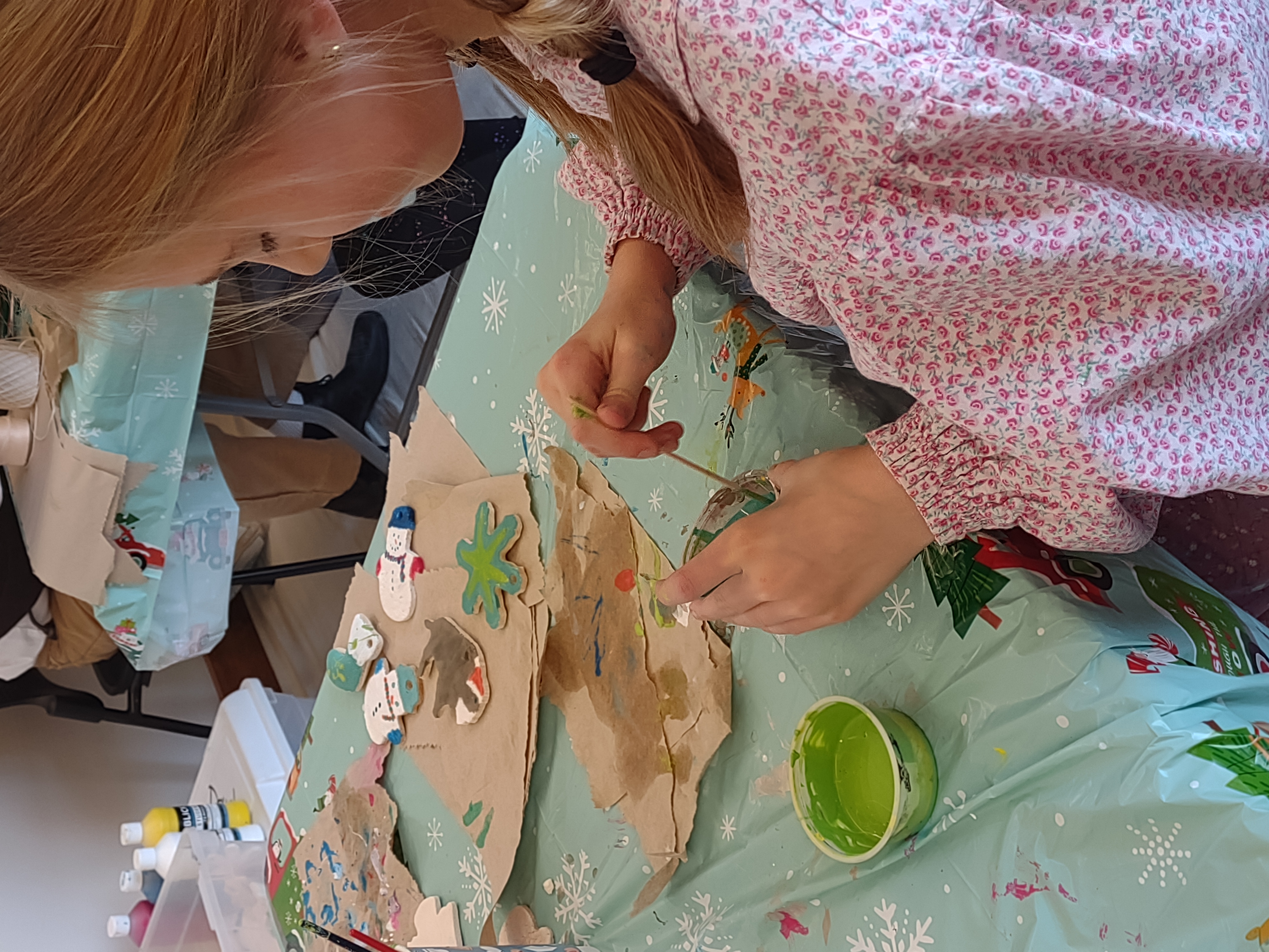 A girl holds a paintbrush and small container of paint.
