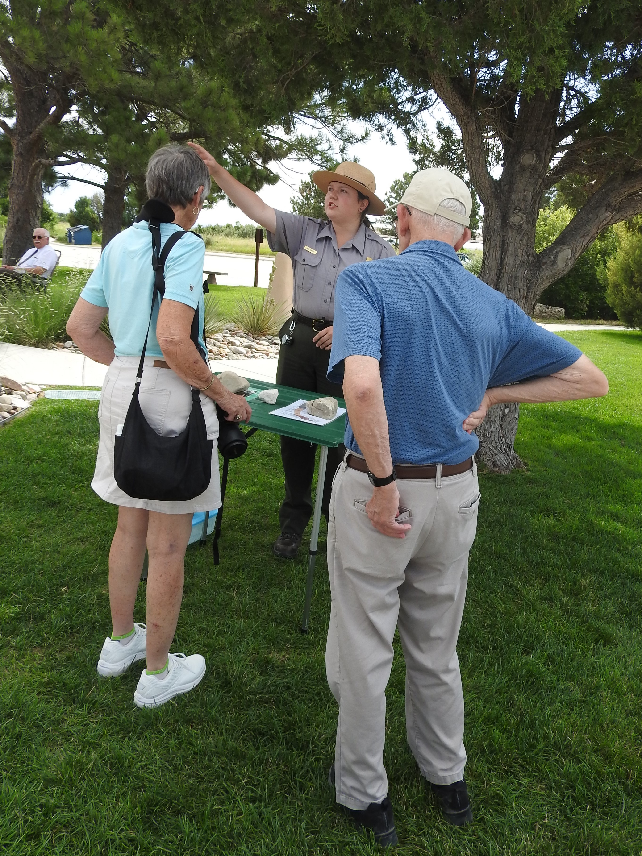 A park ranger points as she talks to two visitors on a grassy lawn.