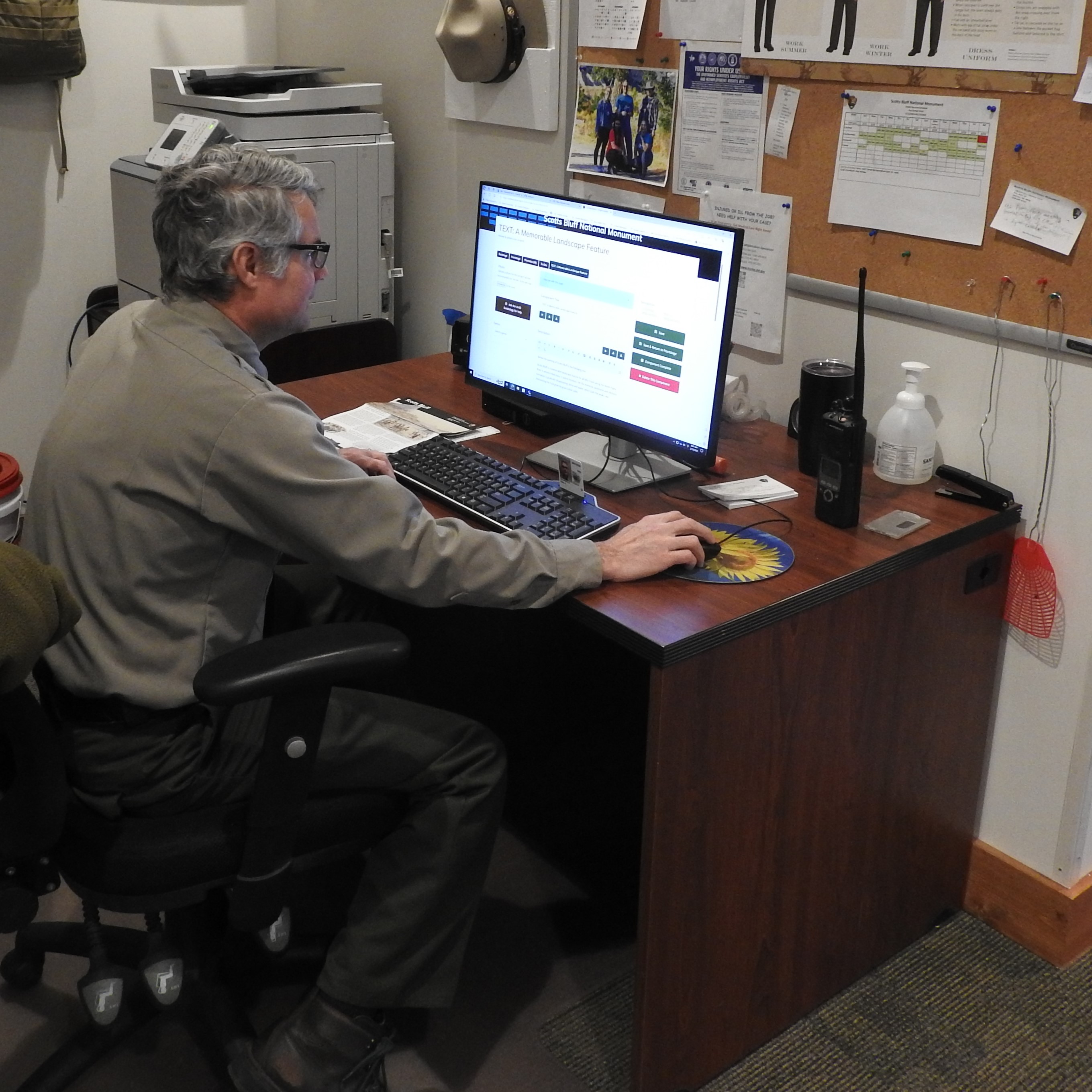 A park ranger sits at a desk, working at a computer.
