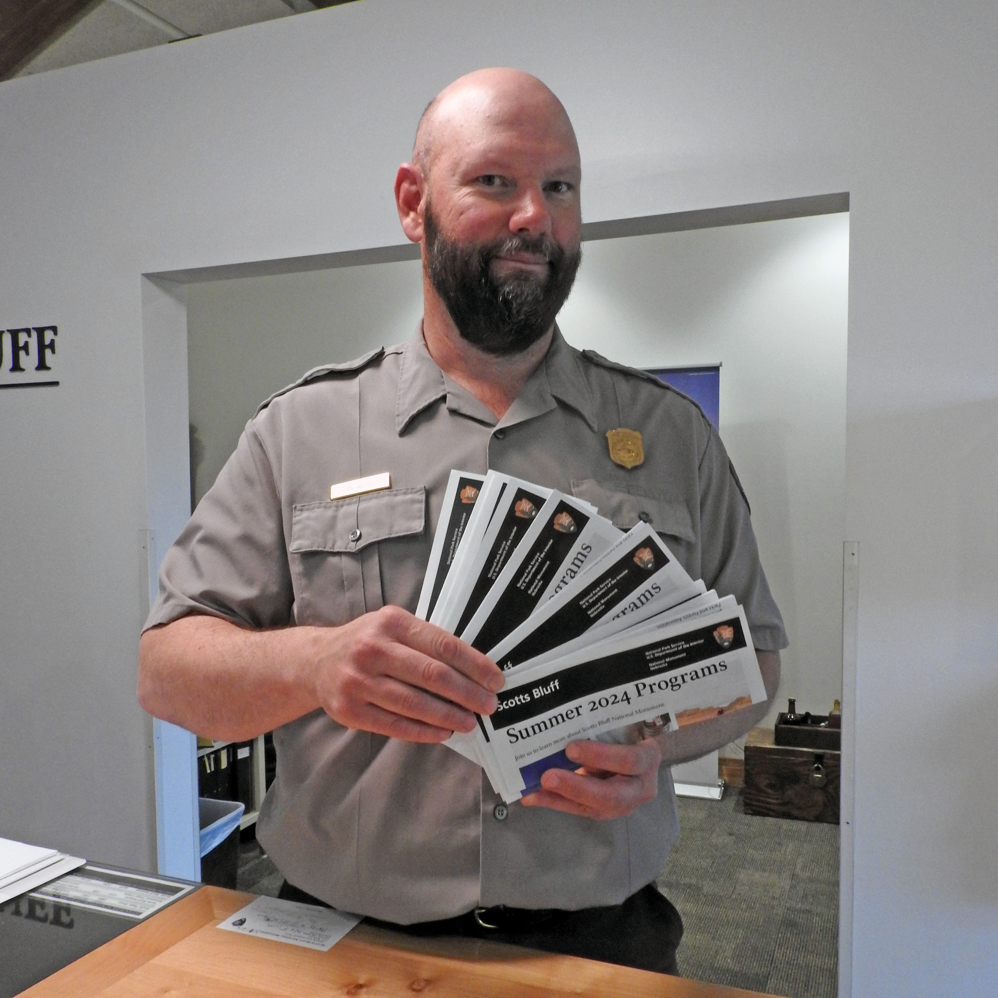 A park ranger stands at a desk holding brochures that are fanned out.
