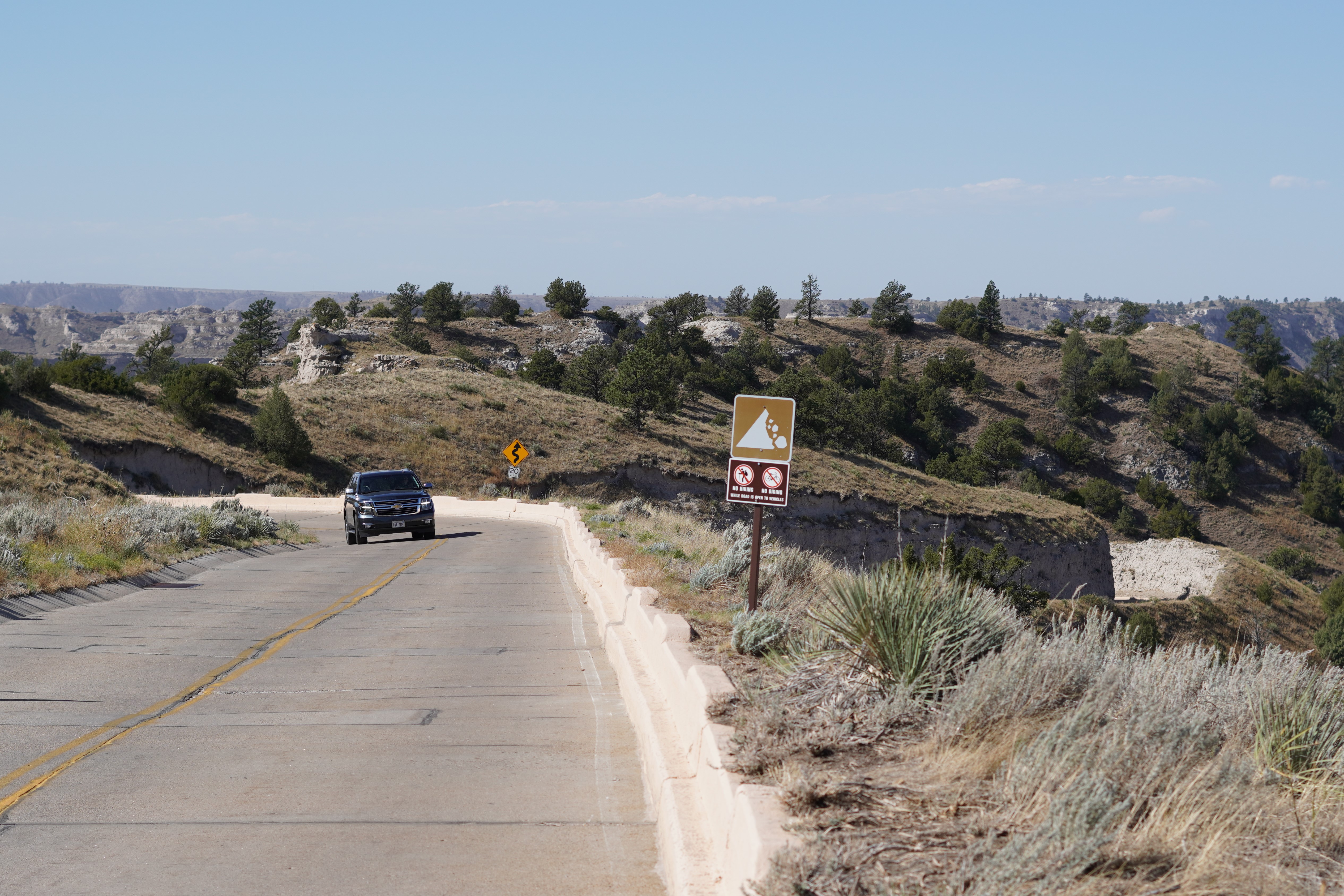 A vehicle drives on a concrete-surfaced road with bluffs in the background.