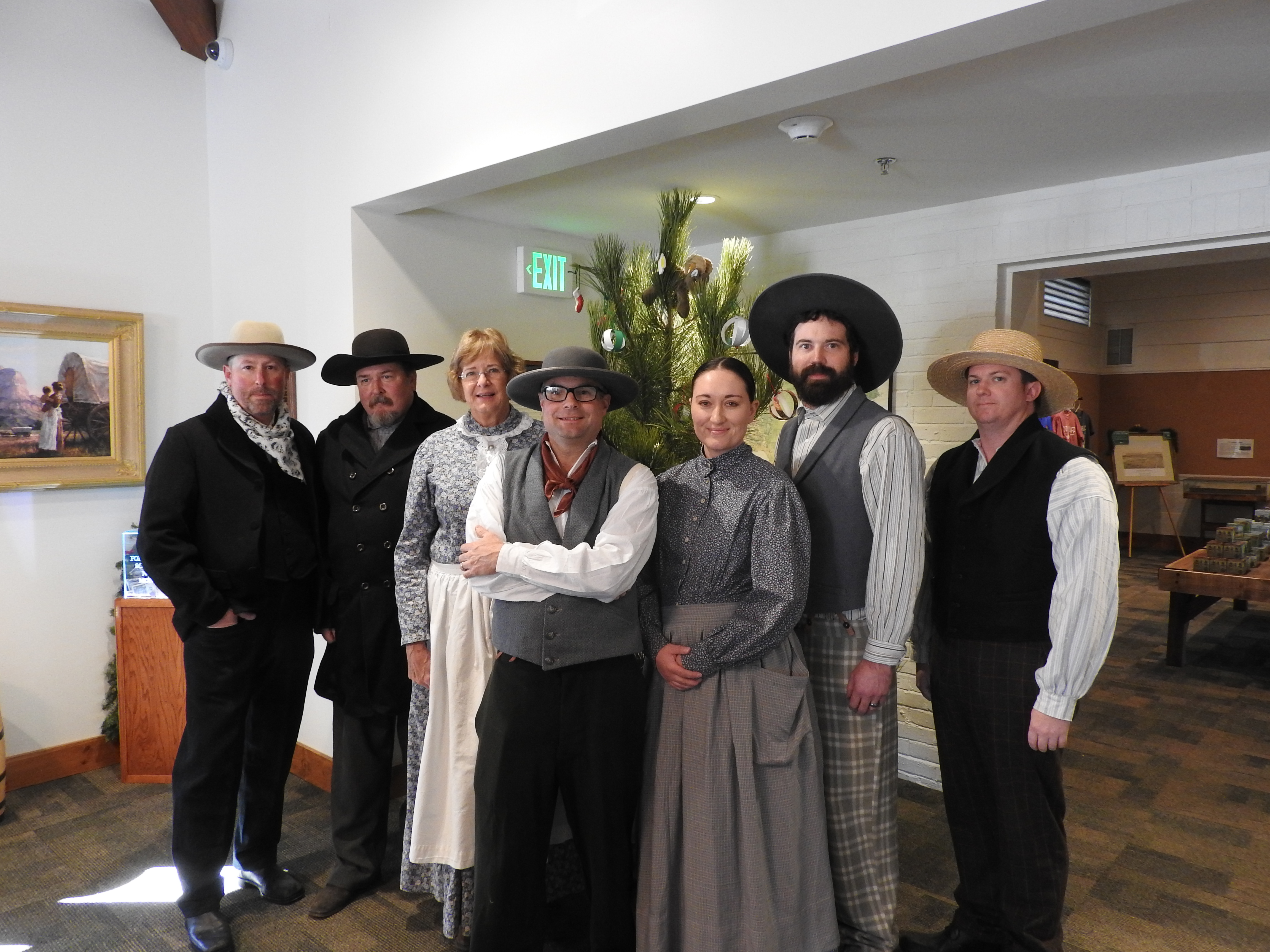 A group of people dressed in clothing of the 1850s stands in front of a Christmas tree.