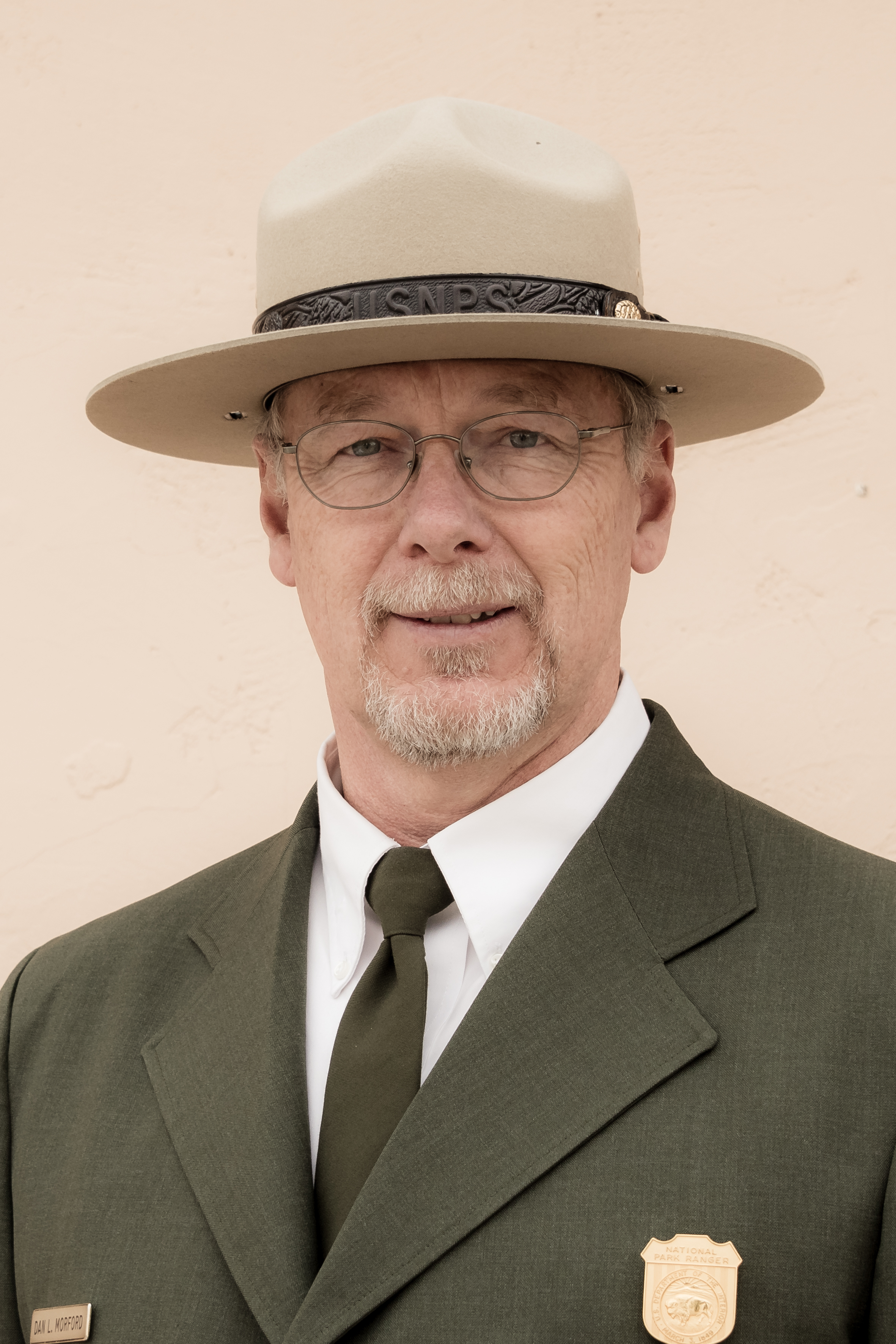 A man wearing the uniform of a National Park Ranger smiles.