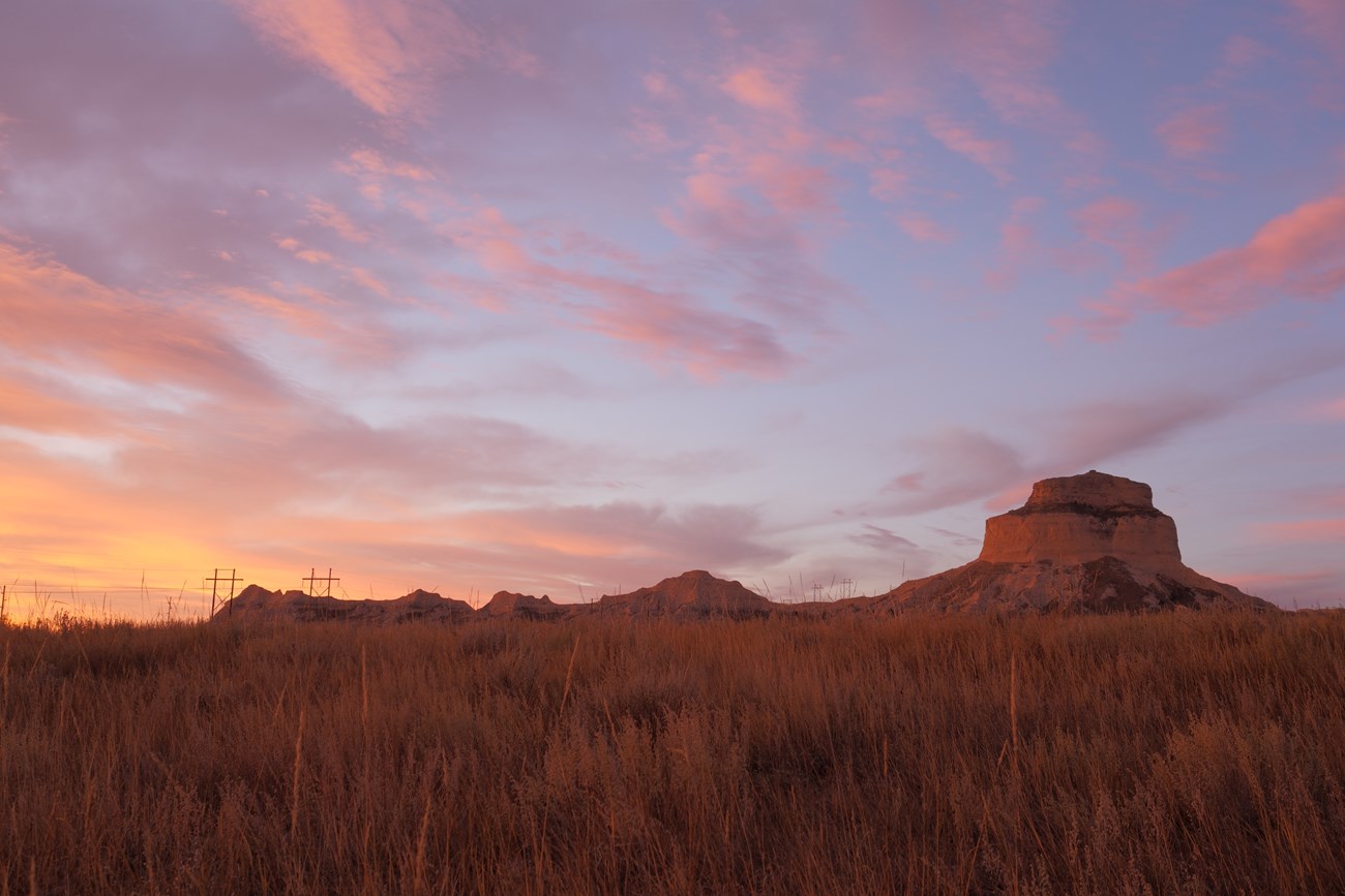 A sandstone butte with a colorful, pink sunrise in the sky above.