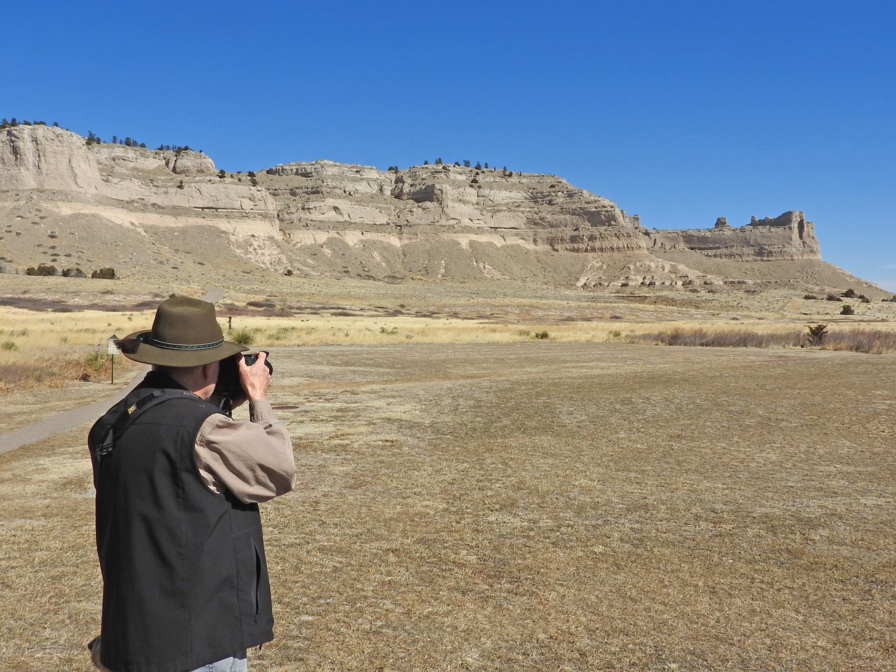 A man takes a photo of distant bluffs with a digital SLR camera.