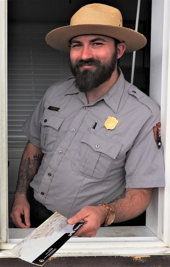 A park ranger leans out of an entrance booth holding a brochure.