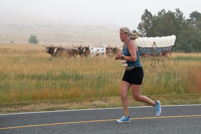 A woman runs past a covered wagon.