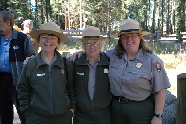 In foreground, three rangers smiling together with forest in the background