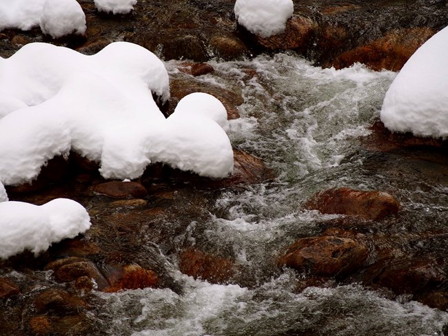 Closeup of flowing water in a river with snow along river bank.