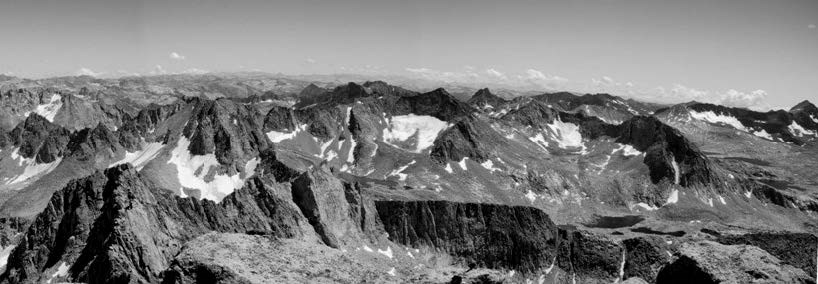 Black and white photo of a rugged mountain range with small white patches of snow and ice scattered across the range.