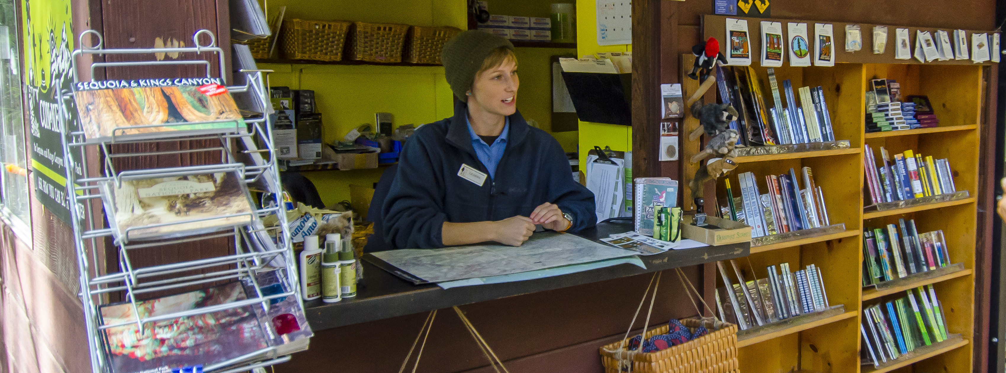 A woman in uniform sits near shelves with books and other sales items