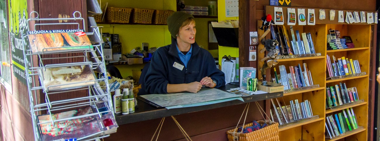 A woman in uniform sits near shelves with books and other sales items