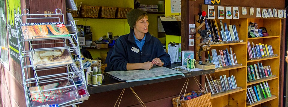 A woman in uniform sits near shelves with books and other sales items