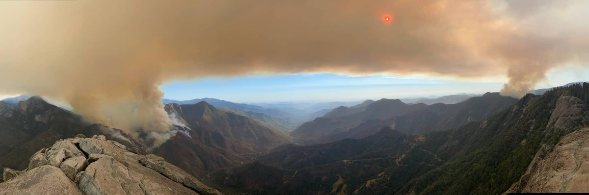 Distant mountains are framed on the left and right by plumes of smoke from wildfires. A halo of smoke covers the horizon.