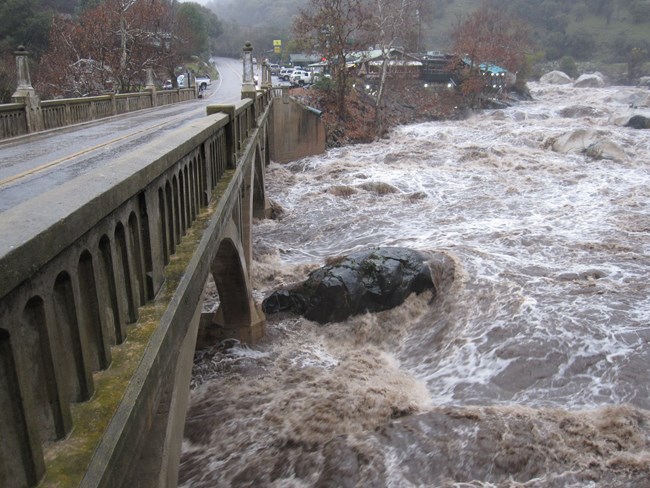 Muddy, high river water rushes downstream past a riverside restaurant and under a bridge in December 2010.