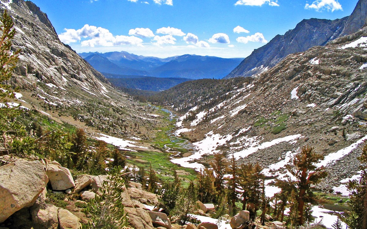 a mountainous u-shaped valley with scattered snow and trees