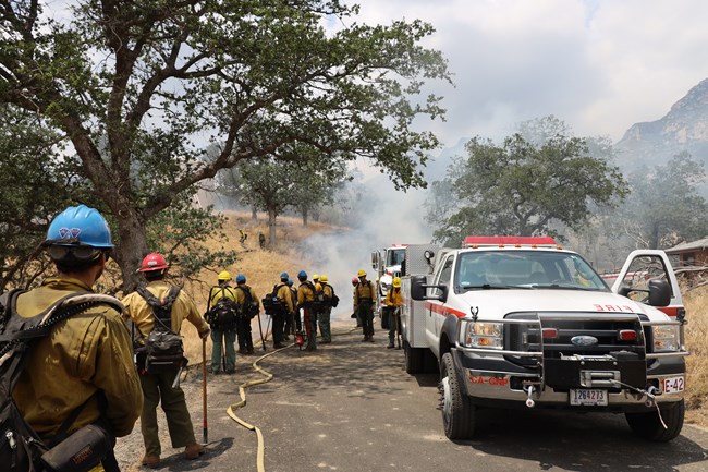 People in hard hats and yellow shirts in a smoky scene near a white truck with red marks on it