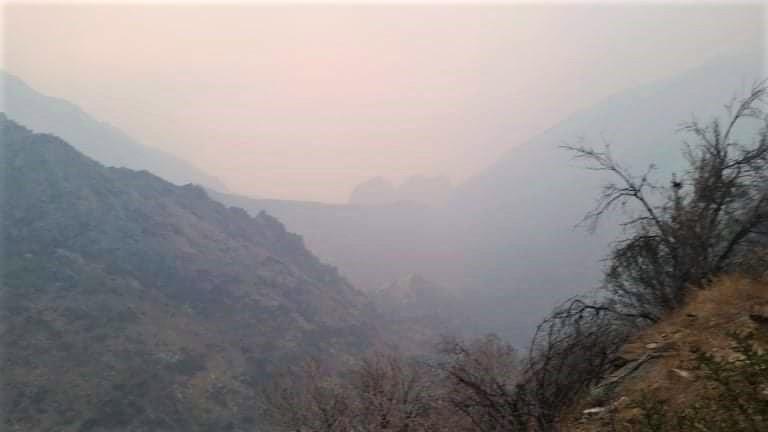 Mountains and a V-shaped canon shrouded in grey-blue smoke.