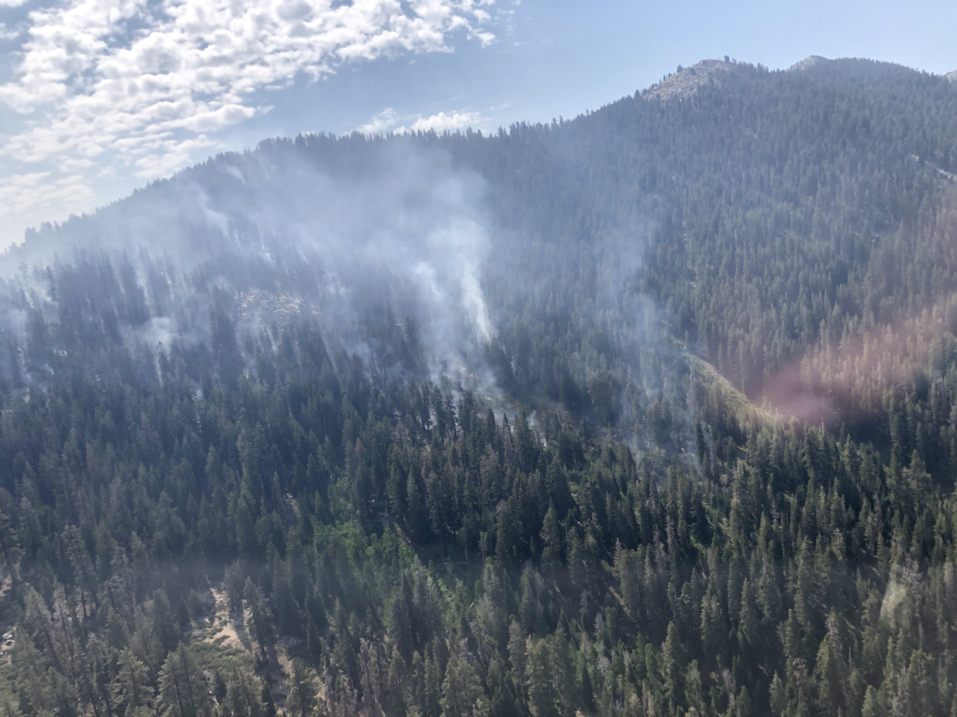 Smoke rises from a rugged forested mountainside