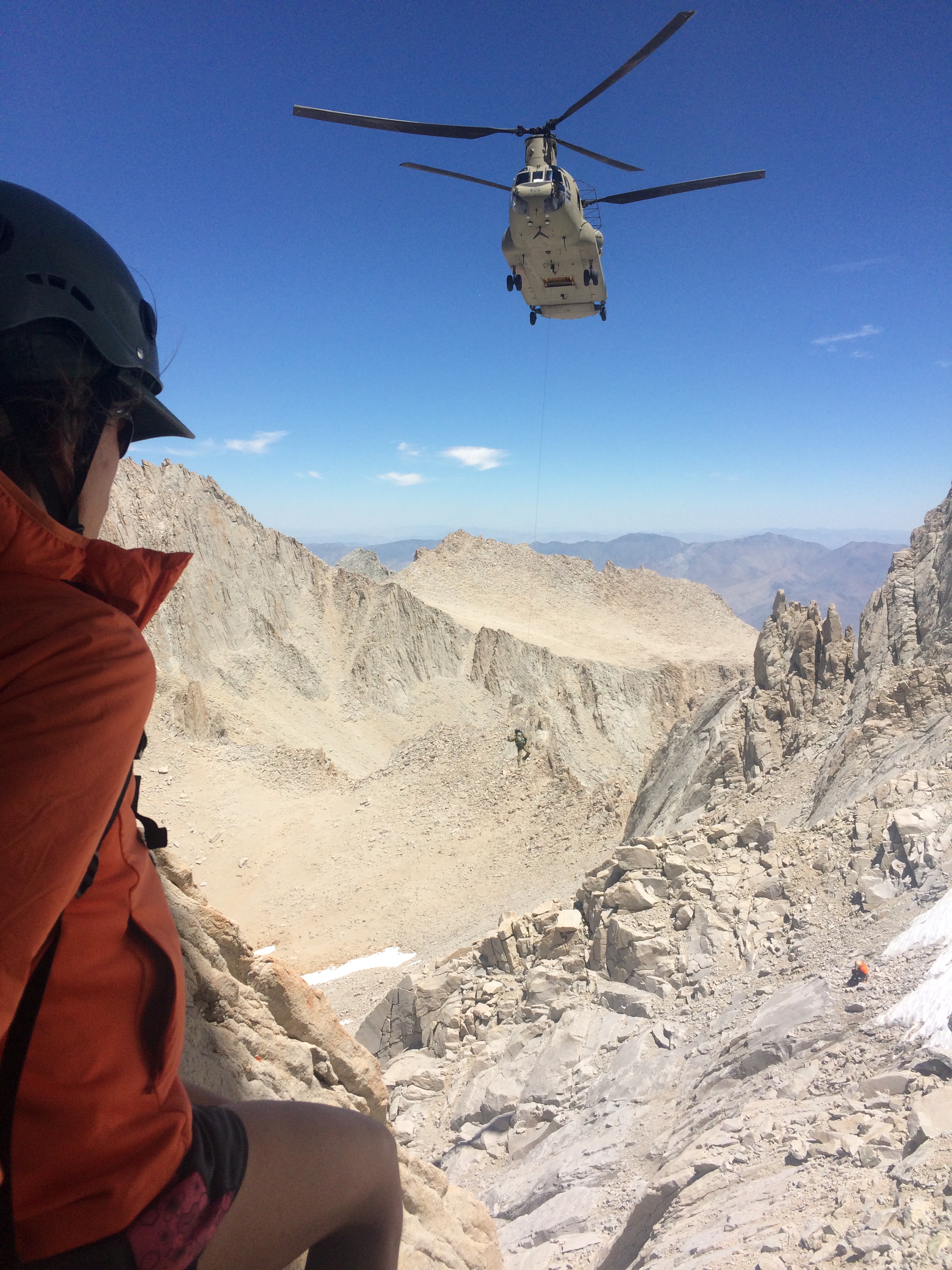 The search for missing hiker John Lee continues. This photo shows a searcher on a mountain in the foreground and a helicopter flying in the background. Photo courtesy of Inyo County Search and Rescue.