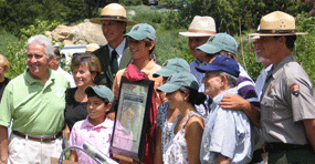 Krebs family and event speakers standing around a map of the John Krebs Wilderness.